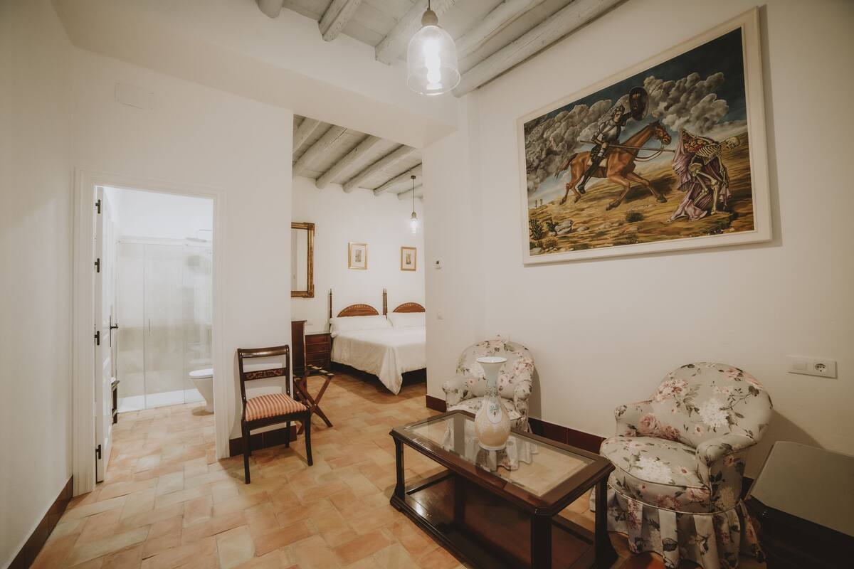 A room with a bed, a chair, a table, and a painting on the wall.