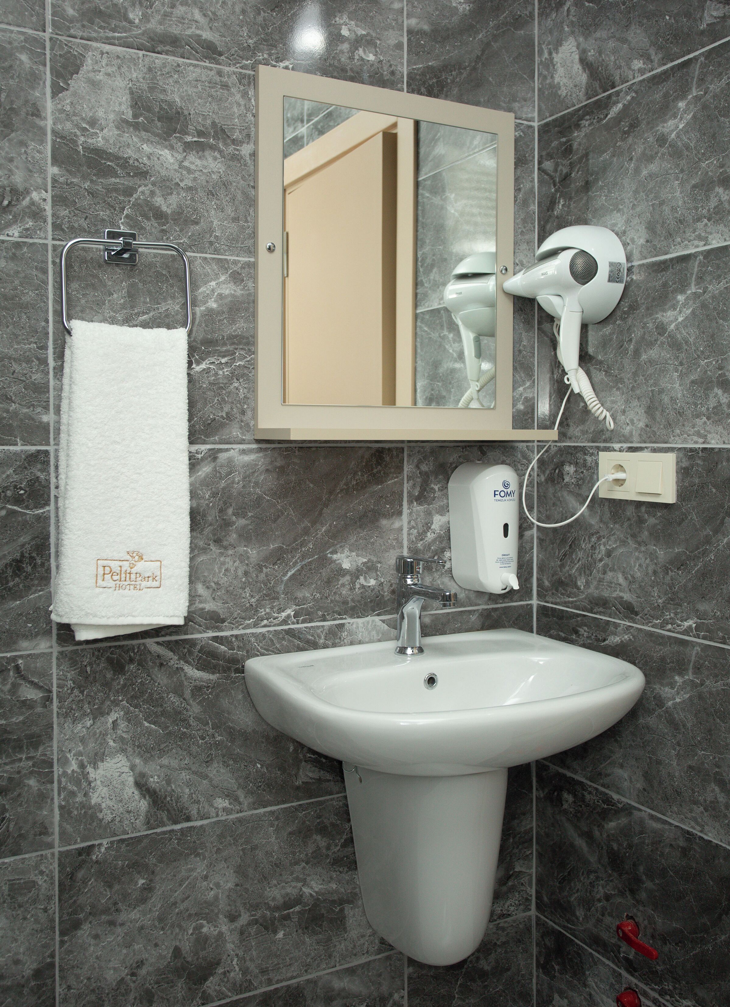 A bathroom with a white sink, a towel rack with a white towel, a hairdryer, and a mirror.