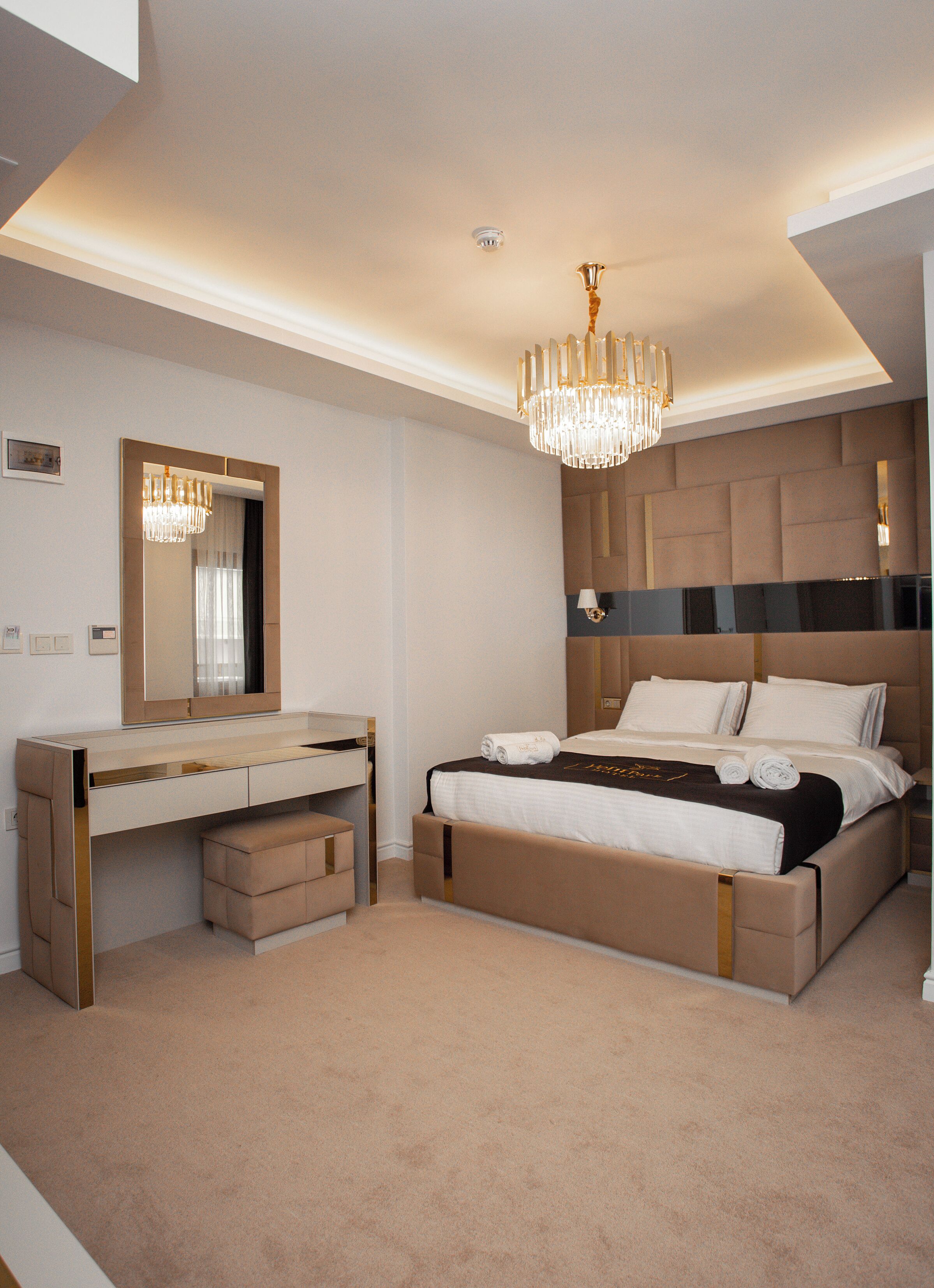 A modern bedroom with a large bed, a vanity with a mirror, and a chandelier.