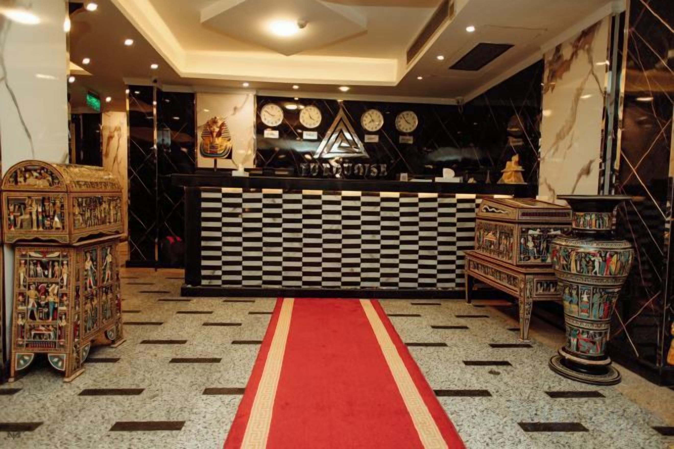A hotel lobby with a checkered floor, a red carpet, and a reception desk.