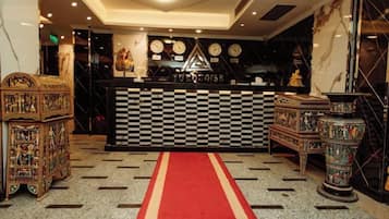 A hotel lobby with a checkered floor, a red carpet, and a reception desk.