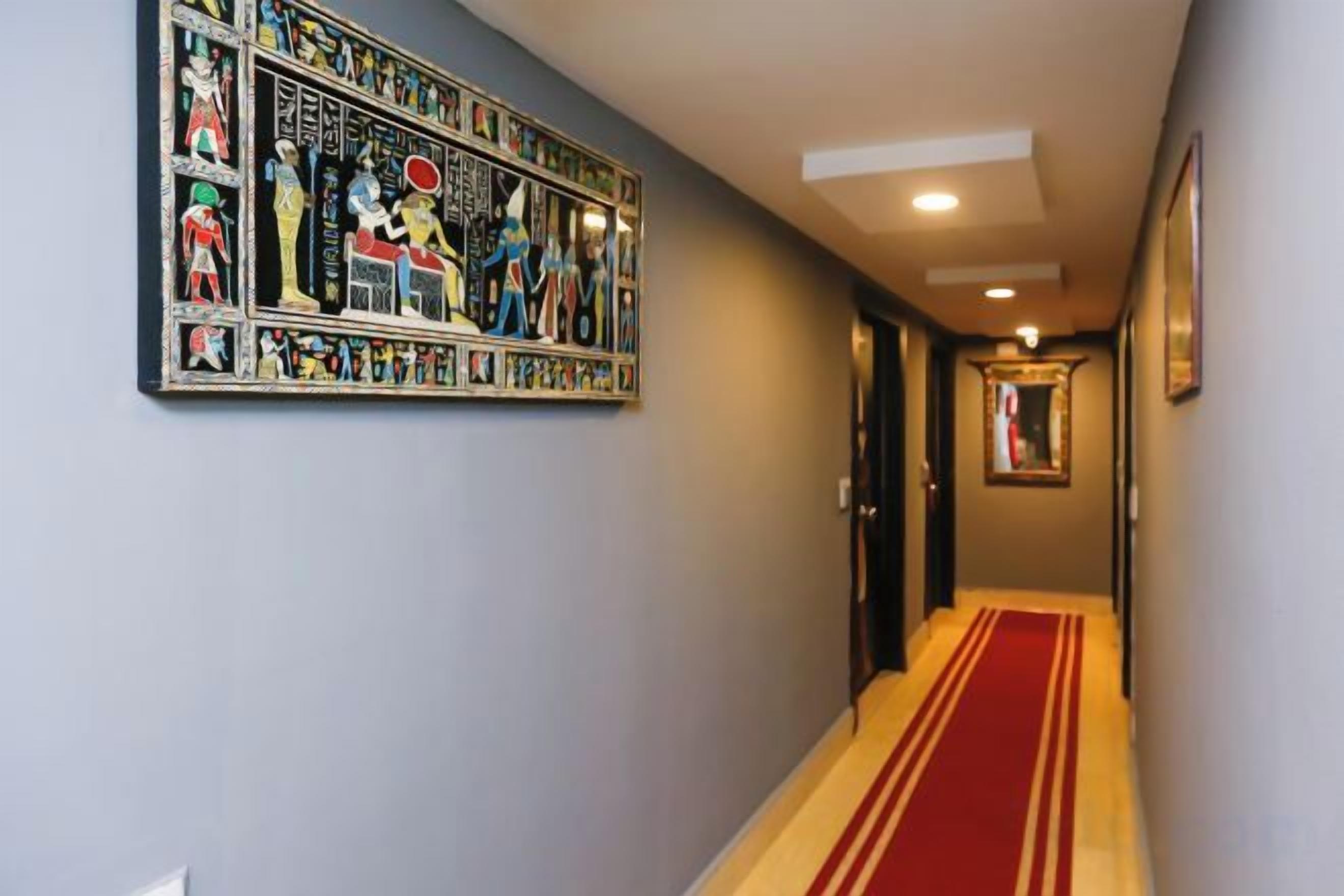 Un pasillo con alfombra roja, una obra de arte en la pared y una puerta al final.