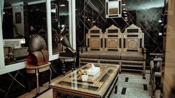 A room with a traditional sofa, a glass-top coffee table, and ornate wall decorations.
