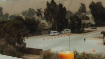 A glass of orange juice on a table with a view of a desert landscape and a road in the background.