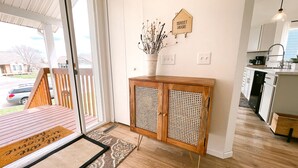 Eine moderne Küche mit weißen Schränken, einem Holzschrank mit Rattanfront, einem Schild mit der Aufschrift 'sweet home' und Blick ins Freie.