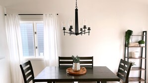 Ein Essbereich mit einem dunklen Holztisch, vier Stühlen, einer Kandelaber und einem Blumentopf auf einem Regal.