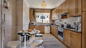 Een moderne keuken met houten kastjes, een eethoek met een tafel en stoelen, en uitzicht door het raam.