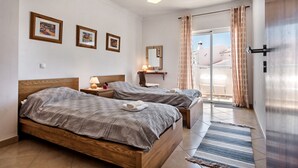 Een hotelkamer met twee houten bedden, een groot raam met gordijnen, een spiegel en kunst aan de muur.