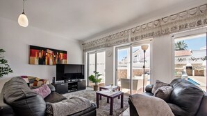 Een moderne woonkamer met een flatscreen televisie, leren banken, een salontafel en een groot raam met uitzicht op een zwembad en terras.