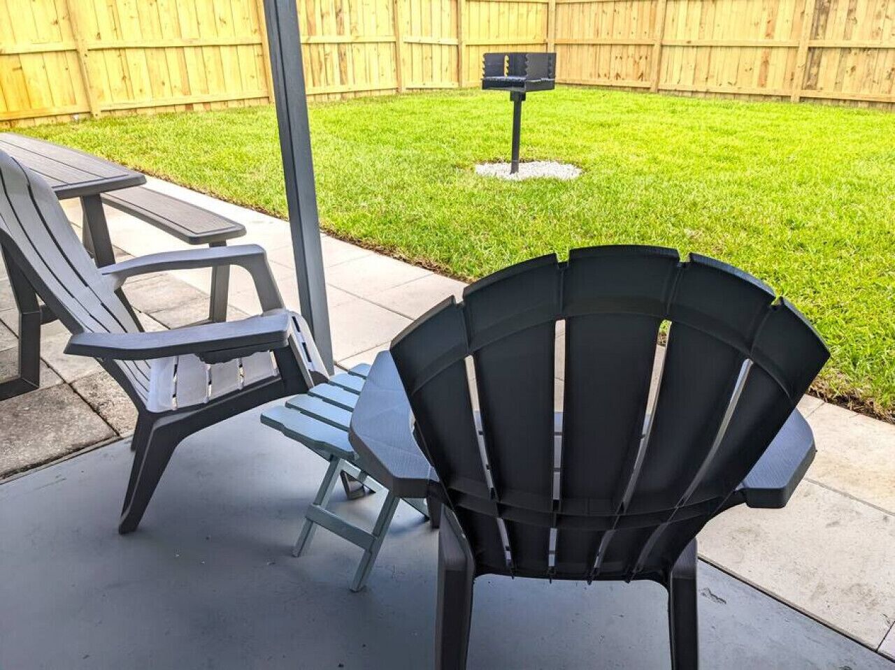 Two Adirondack chairs and a picnic table in a backyard with a wooden fence and a mailbox.
