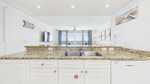 Cocina moderna con encimeras de granito, muebles de color blanco y pileta de acero inoxidable, además de lavavajillas Whirlpool.