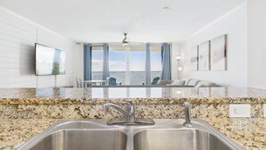 Cocina con encimeras de granito, lavamanos de acero inoxidable y vista al océano a través de amplios ventanales.