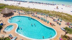 Una piscina amplia con varias pistas de natación, rodeada de tumbonas y una estructura con techo de paja.