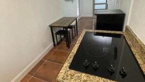 A compact kitchen with a black stovetop, a small dining table, and a TV mounted on the wall.