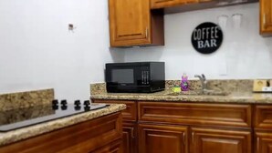 A kitchen with wooden cabinets, a granite countertop, a microwave, and a coffee bar sign.
