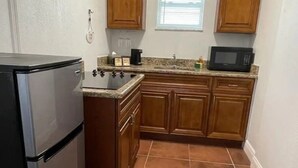 A compact kitchen with wooden cabinets, a built-in microwave, a refrigerator, and a window providing natural light.