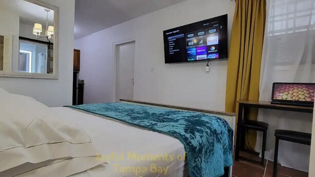 A hotel room with a bed, a TV mounted on the wall, and a desk with a chair.