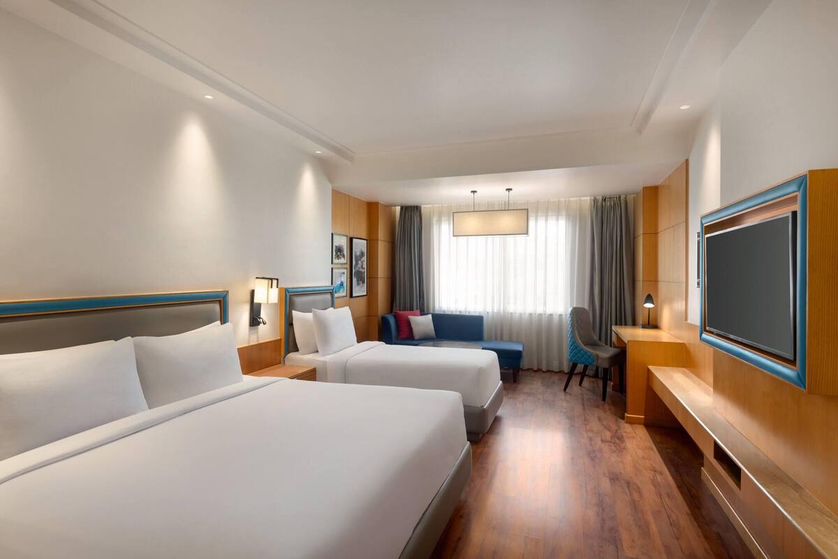 A hotel room with two beds, a desk, a chair, a TV, and a window with curtains.