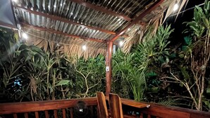 Eine Holzterrasse mit einem Reetdach, umgeben von üppigem Grün.