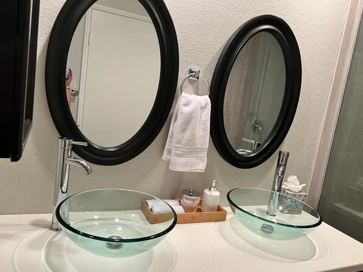 Une salle de bain avec deux miroirs ronds, un lavabo en verre en forme de bol et un porte-serviettes.