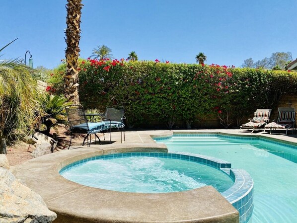 Una piscina con hidromasaje, rodeada de sillones de descanso y un jardín exuberante.