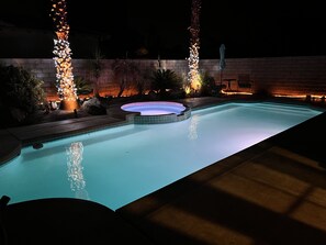 A swimming pool with a hot tub, surrounded by decorative lighting and plants.
