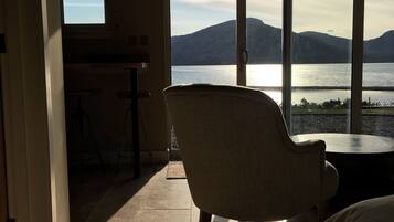 A room with a view of a lake and mountains, a chair, and a bed.