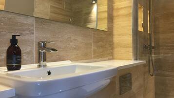 A modern bathroom with a white sink, a handheld showerhead, and a bottle of liquid soap.