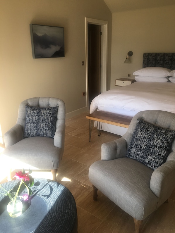 A hotel room with a bed, two armchairs, a small table with a vase of flowers, a painting on the wall, and a door leading to another room. - Kirkton Bay House Bed and Breakfast (Kyle)