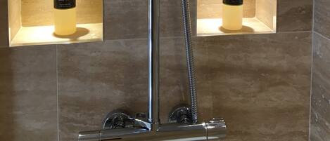 A modern shower with a handheld showerhead and a rain shower attachment. There are two shelves with bottles of body wash and shampoo.