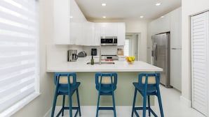 Una cocina moderna con armarios blancos, un refrigerador de acero inoxidable y una isla central con taburetes de bar.
