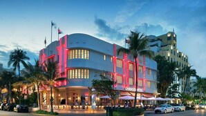 Un hotel con fachada curva, palmeras y mesas al aire libre.