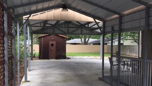 A covered outdoor area with a concrete floor, metal railings, and a small shed in the background.