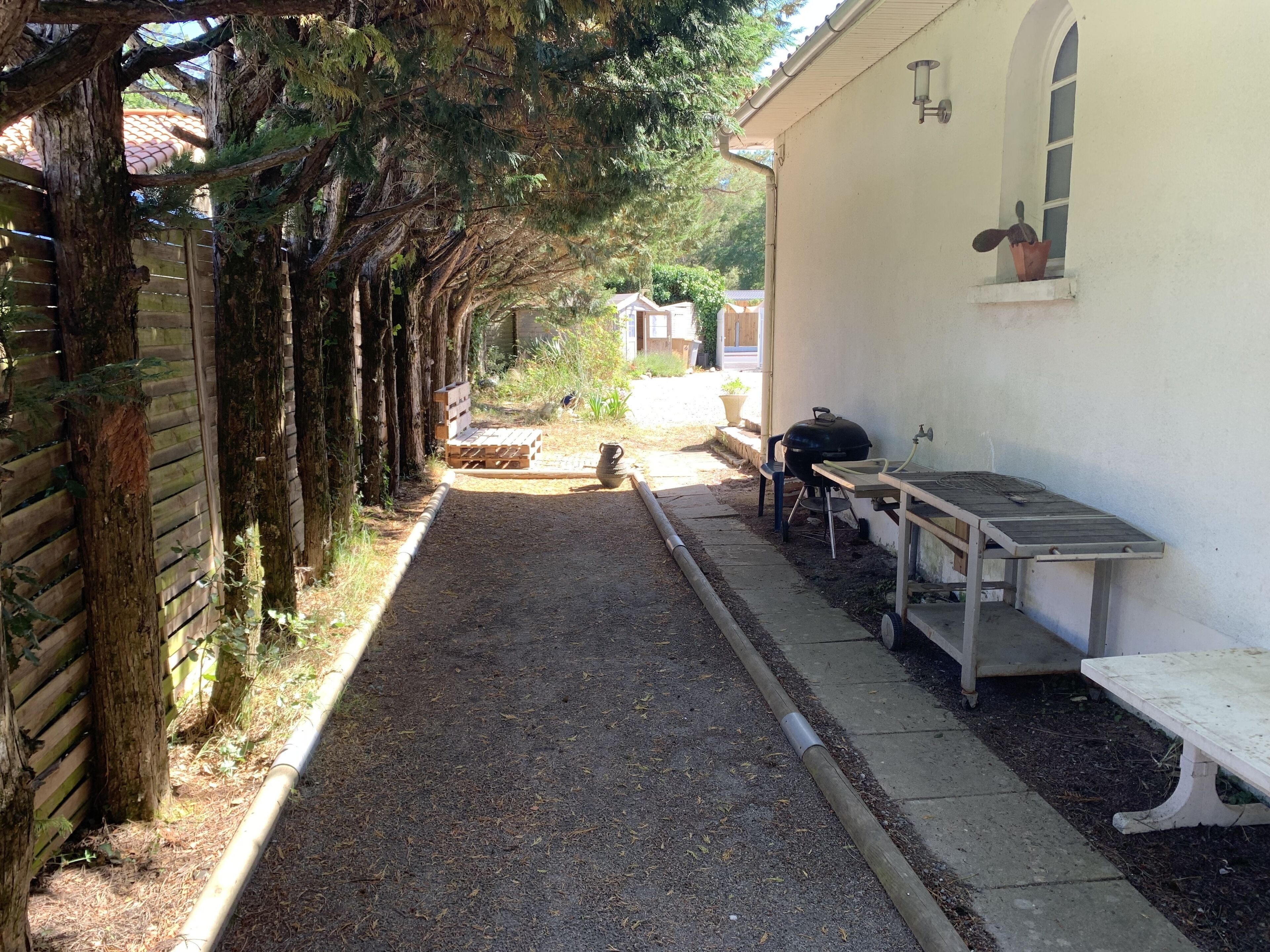 Un sentier étroit bordé d’arbres, qui mène à un bâtiment doté d’un espace barbecue et d’un banc.