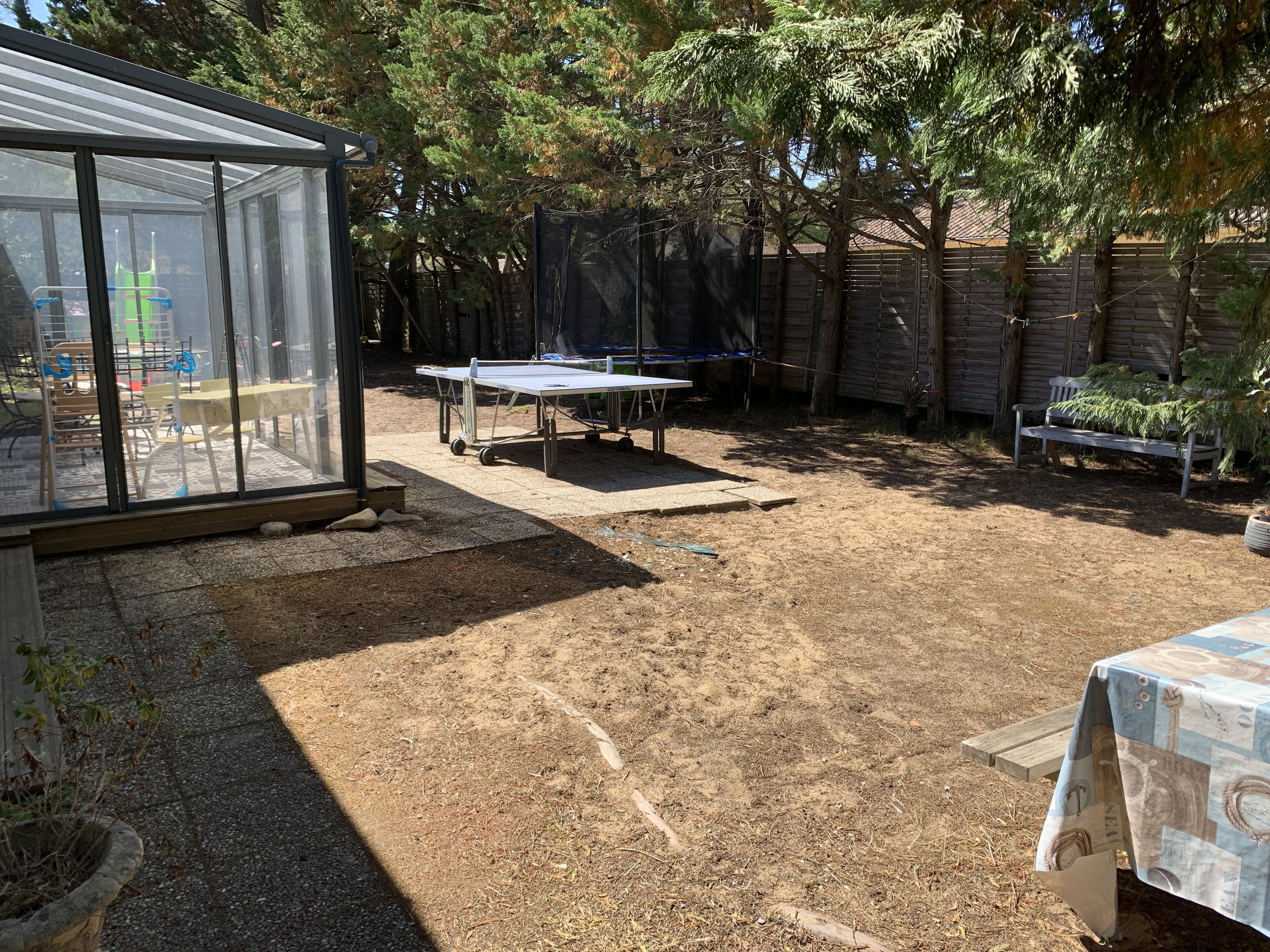 Ein Garten mit einem Tischtennisplatten, einer überdachten Sitzgruppe und einem Gewächshaus.
