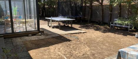 Ein Garten mit einem Tischtennisplatten, einer überdachten Sitzgruppe und einem Gewächshaus.