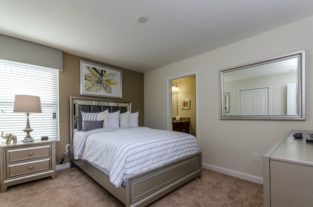 A bedroom with a bed, bedside table, lamp, and a large mirror.