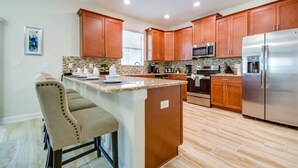 A modern kitchen with wooden cabinets, a stainless steel refrigerator, and a granite countertop.