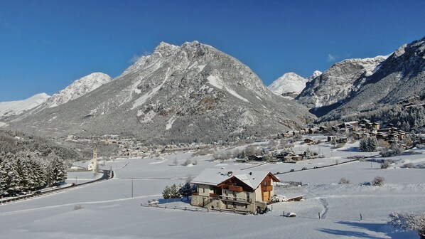 A snow-covered mountain village with traditional wooden houses, a church, and a clear blue sky. - AGRITURISMO SAN GALLO (Bormio)