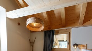 A wooden cabin interior with a bed, two chairs, a wooden stool, a cowhide rug, and a hanging light fixture. - AGRITURISMO SAN GALLO (Bormio)