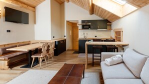 A cozy, open-plan living and dining area with wooden furniture, a flat-screen TV mounted on the wall, and a kitchen with modern appliances. - AGRITURISMO SAN GALLO (Bormio)