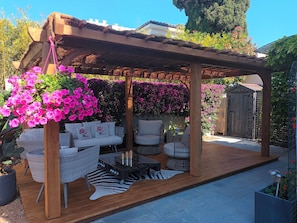 En træpergola med siddepladser, omgivet af blomstrende blomster og en træterrasse.
