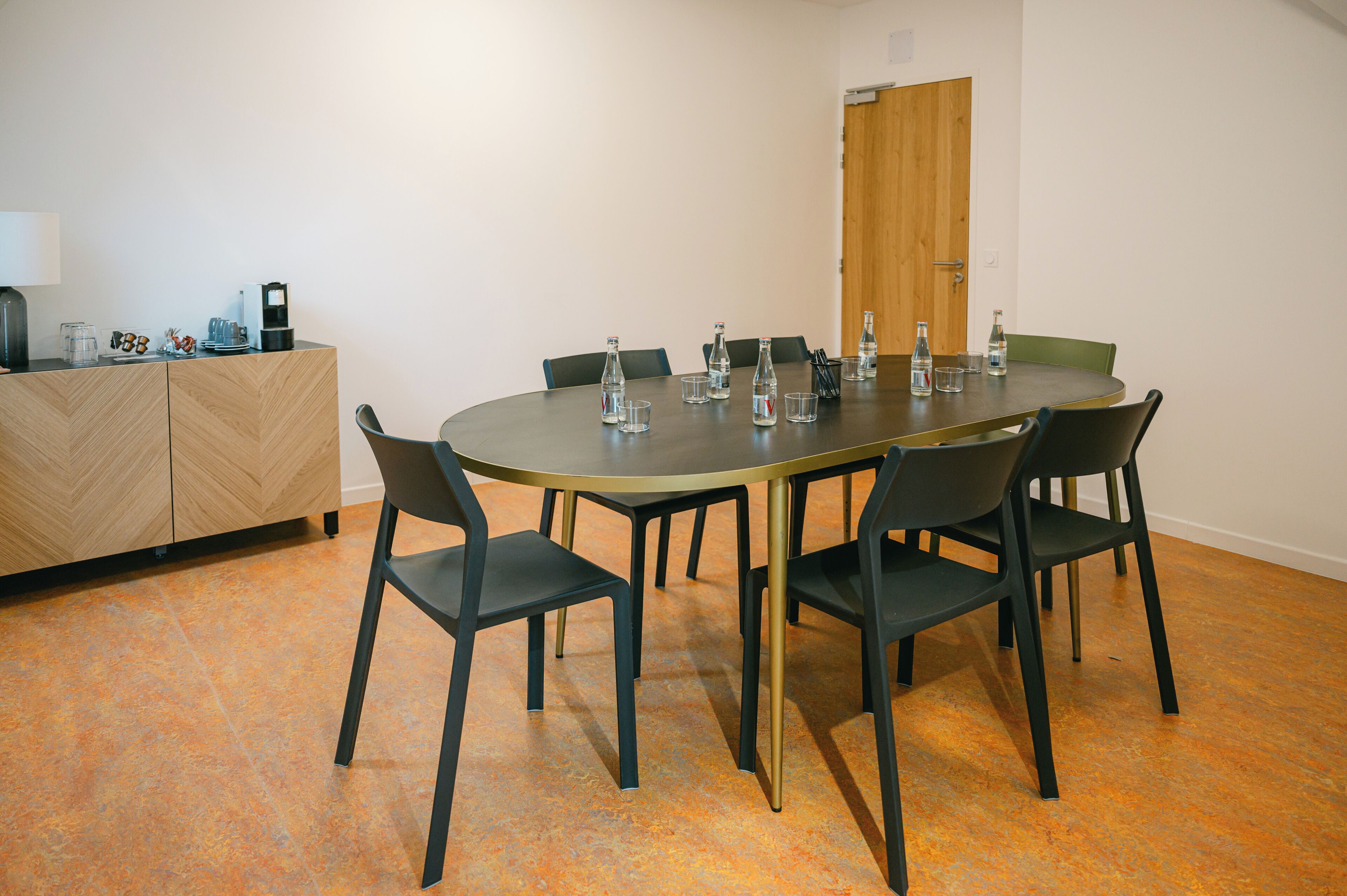 A conference room with a round table, six chairs, and a coffee station.
