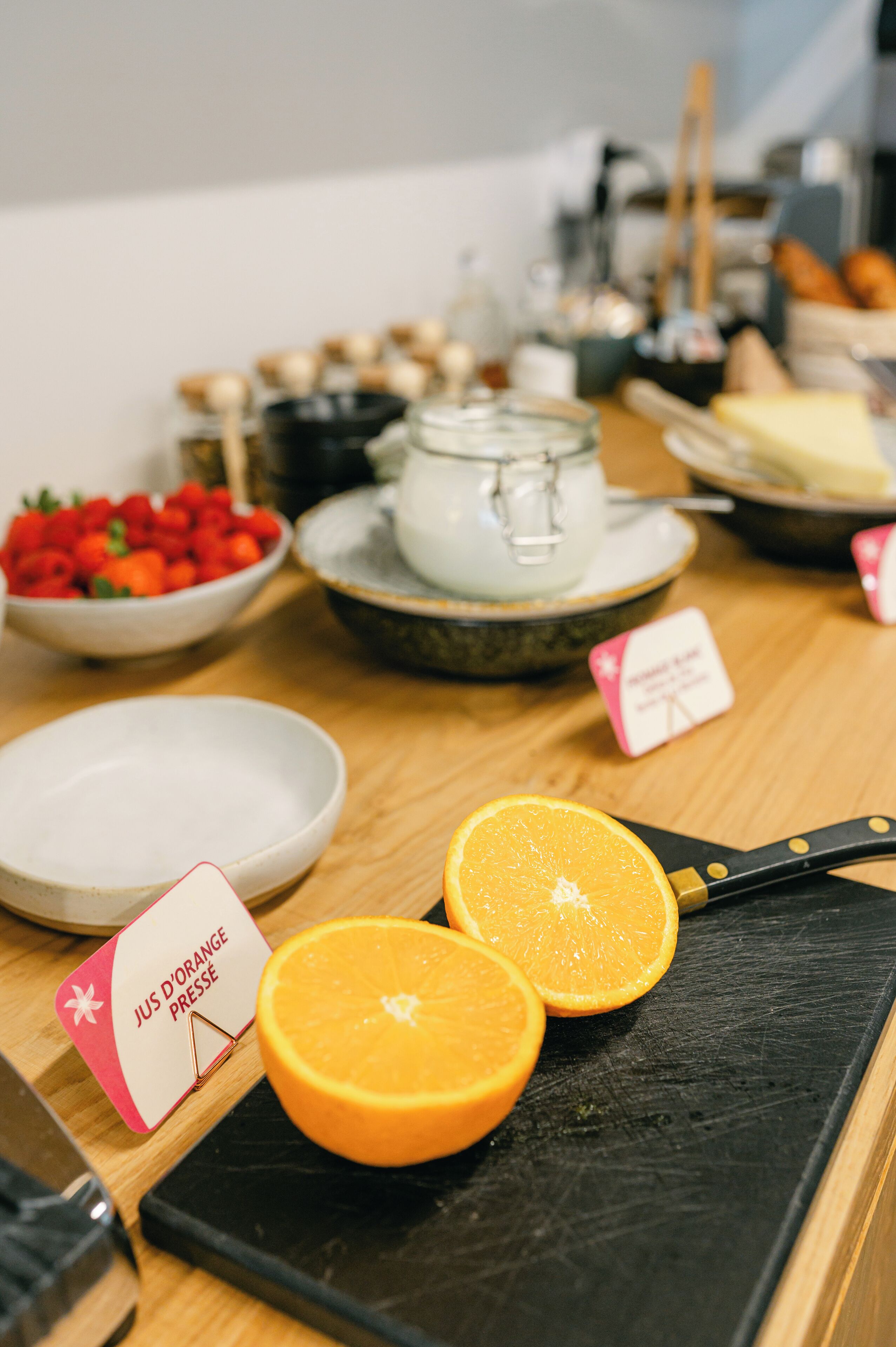 Aamiainen tarjoillaan buffetpöydästä, ja siellä on monenlaista syötävää sekä kyltti, jossa kerrotaan, että tarjolla on appelsiinimehua.