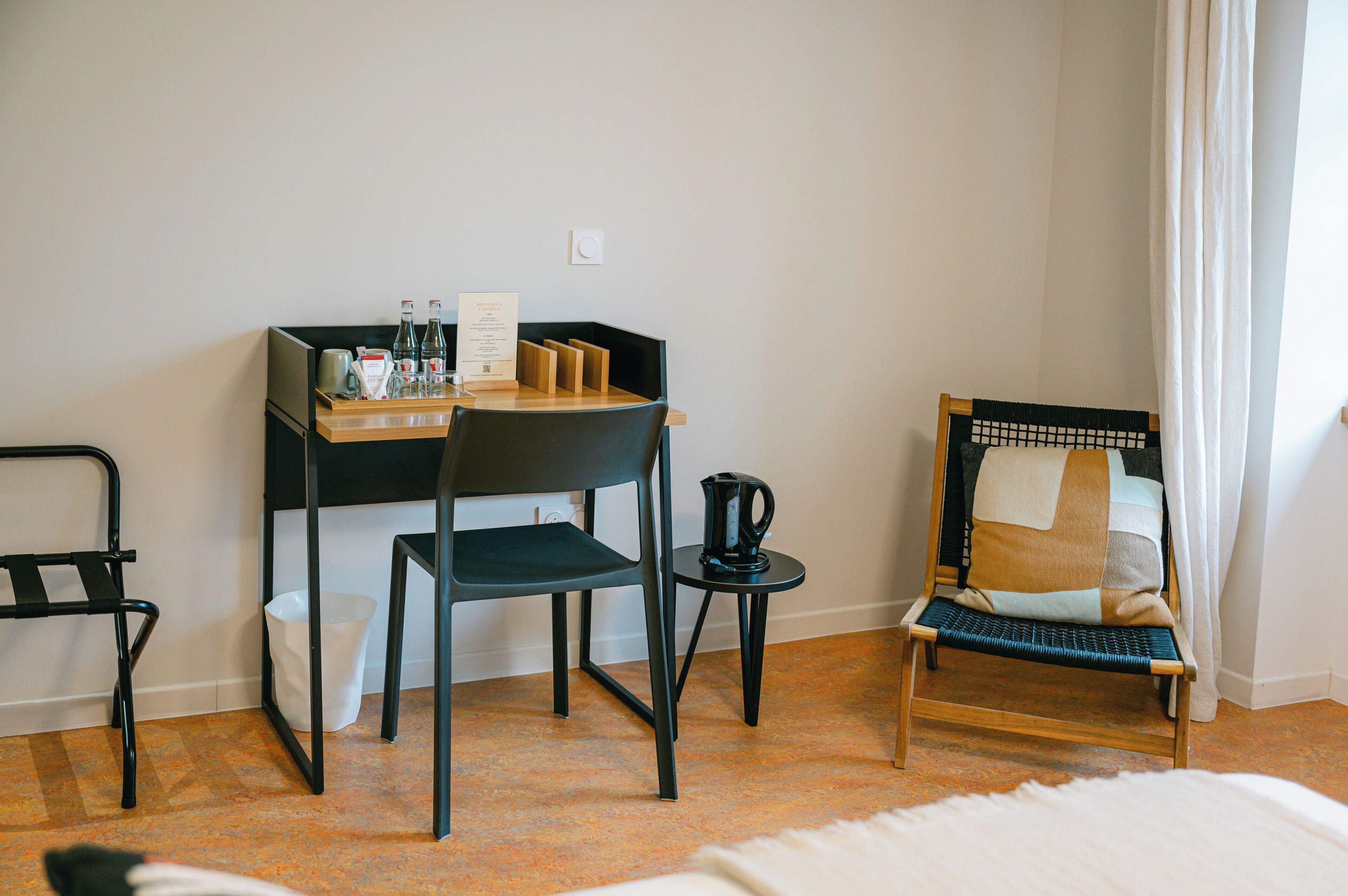 Een hotelkamer met een bureau, een stoel, een bed en een klein tafeltje met een waterkoker.