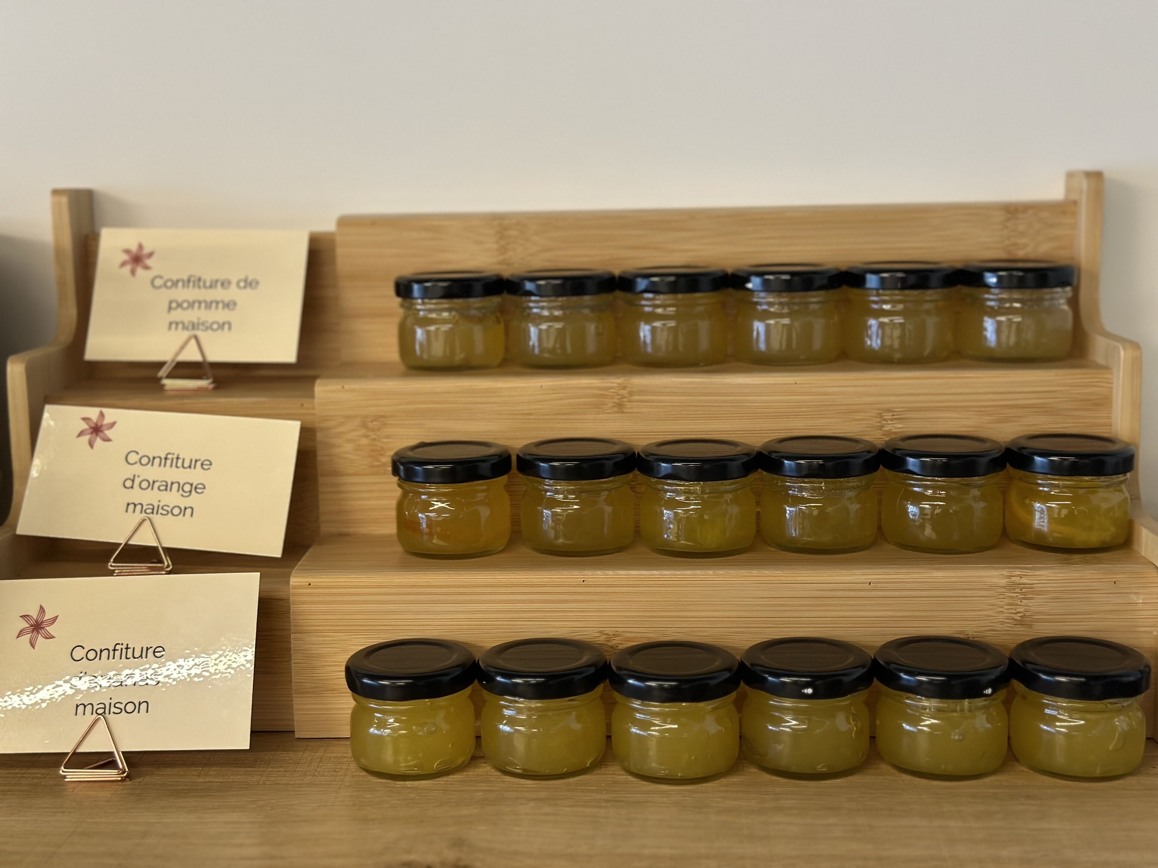 Una exhibición de conservas caseras en frascos de vidrio con tapas negras, dispuestas sobre estantes de madera.