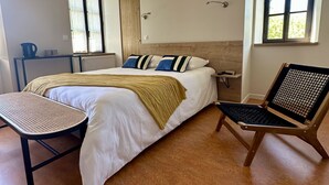 Un dormitorio moderno con una cama grande, una mesita, una silla y un ventanal.