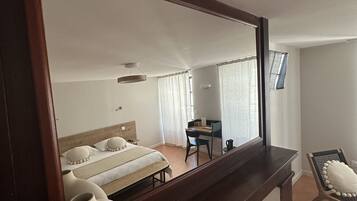 Une chambre d’hôtel avec un grand miroir, un lit avec des oreillers, un bureau avec une chaise et une vue sur l’extérieur par la fenêtre.