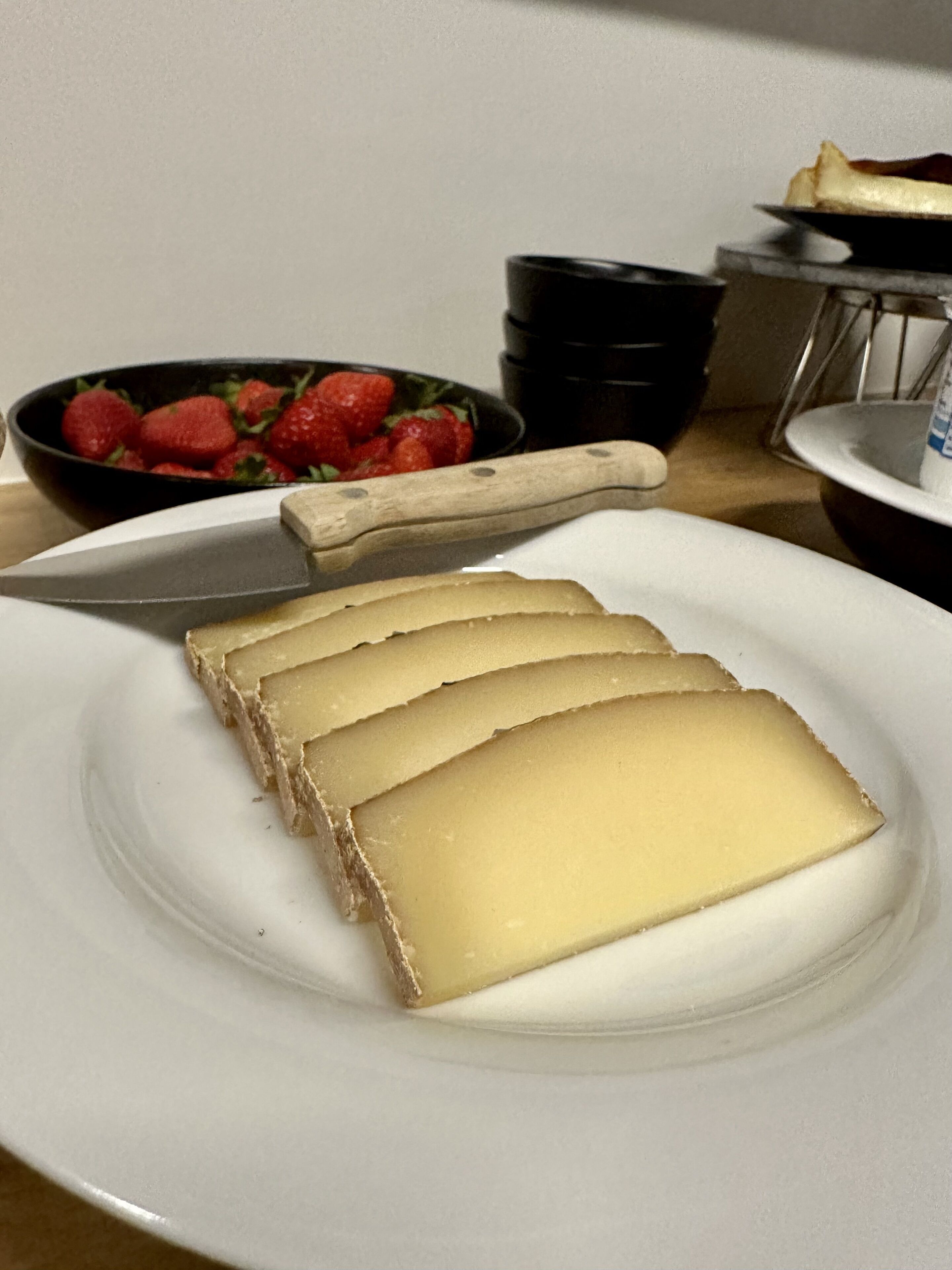 Un plato con rebanadas de queso, un bol de fresas y un cuchillo sobre una mesa.