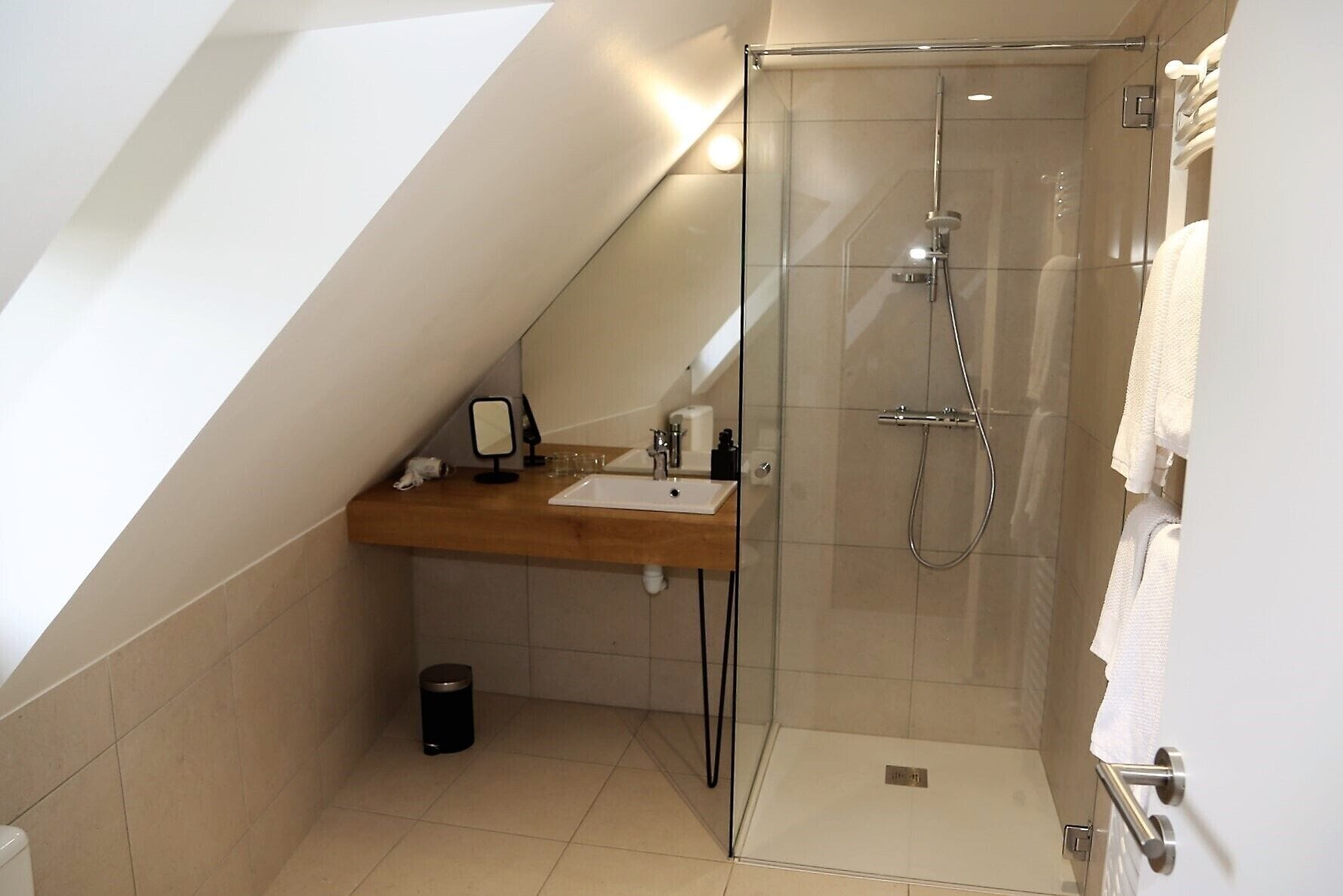 A modern bathroom with a glass shower enclosure, a wooden vanity, and a small trash bin.